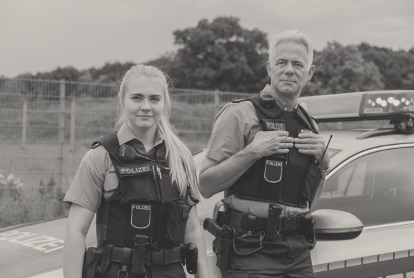 Photography of a German police woman and a police man leaning towards a car